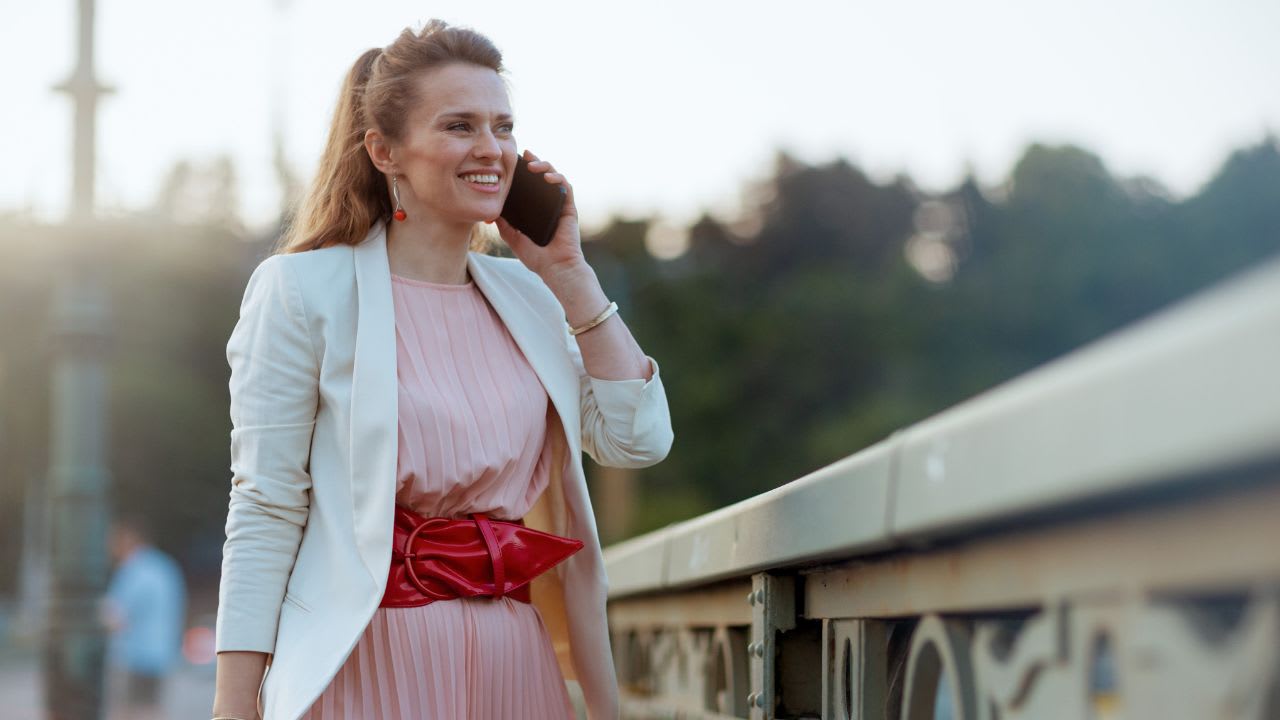 Smiling elegant 40 years old woman in city talking on phone. Date night outfits for 40 year olds